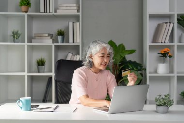 Yaşlı bir kadın, rahat bir ofis ortamında kredi kartını kullanarak online alışveriş yapmaktan zevk alır..