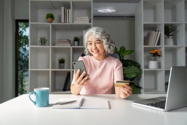 Yaşlı bir kadın, teknoloji ve yaşam tarzının karışımını gösteren kredi kartını kullanarak online alışveriş yapmaktan hoşlanıyor..