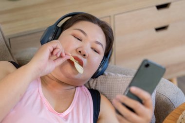 Bir kadın evinde rahatlarken tatlı ikramlara dalıp rahatlık ve ağırlık arasındaki ilişkiyi ön plana çıkarır..