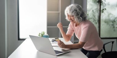 Heyecanlı bir son sınıf öğrencisi başarılı online alışveriş deneyimini kutlarken bir yandan da bilgisayarında ve kredi kartıyla modern bir ev ofisinde oturuyor..