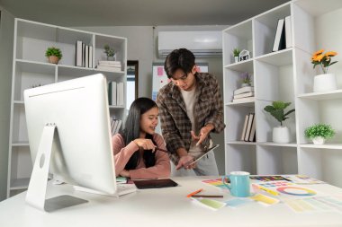 Tasarımcı profesyoneller, şık bir ofiste renkli tasarım malzemeleriyle çevriliyken tablet üzerinde yaratıcı kavramları keşfediyorlar..