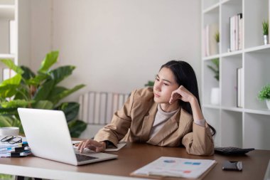 Odaklanmış bir iş kadını, dizüstü bilgisayarını yeşil bir ofis masasında gezdirirken derin düşüncelere dalmış, çenesini eline dayar..