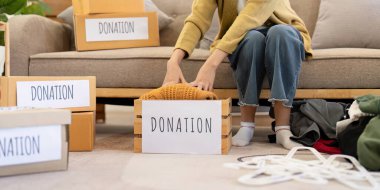 A woman thoughtfully adding a knitted sweater into a donation box while sitting on the floor, creating a tidy space in her inviting living room. clipart