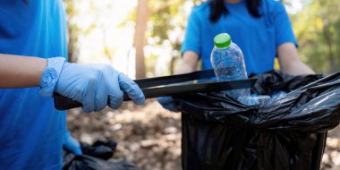 Mavi gömlekli gönüllülerin plastik bir şişeyi almak ve çöp poşetine atmak için maşa kullandıkları yakın plan çekimleri çevresel sorumluluğa olan bağlılıklarını vurguladı..
