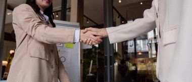 Çağdaş ofis ortamında verimli bir iş görüşmesi sonrasında iki profesyonel kadın el sıkışıyor, ortaklığı ve anlaşmayı sembolize ediyor.