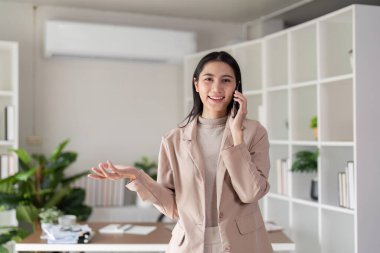 Canlı bir iş kadını telefonuyla konuşuyor. Motivasyon dolu ofisinde bir iş görüşmesi sırasında biriyle el kol hareketi yapıyor..