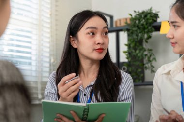 Bir takım tartışmasına katılan odaklanmış bir iş kadını fikirlerini iyi aydınlatılmış, modern bir ofiste bir defterle sunuyor..