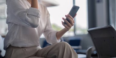 Havaalanı salonunda akıllı telefonuyla meşgul olan bir kadının yakın görüntüsü, uçuşunu beklerken odak ve beklenti ifade ediyor..