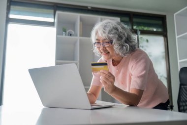 Modern ev ofisinde online alışveriş yapmak için kredi kartını kullanırken heyecanla öne doğru eğilen neşeli bir son sınıf kadını..