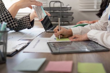 İşbirlikçi bir toplantıda grafikleri analiz eden ve notlar yazan odaklanmış bir grup uzman, çalışma alanlarındaki çizelge ve tabletlerden yararlanıyor.