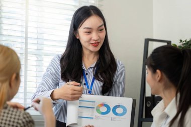 Bir Asyalı profesyonel, ekibine sunduğu bir raporda, modern ofis ortamında işbirliğini teşvik ederek, kendinden emin bir şekilde veri içgörüsü sunuyor..