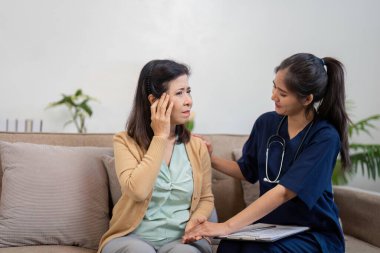Şefkatli bir bakıcı yaşlı bir hastayı nazikçe rahatlatır. Endişe belirtileri gösterir, destekleyici bir ev ortamında güven ve bakım sunar..