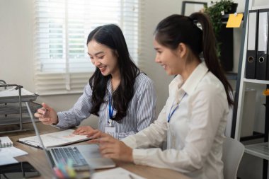 İki iş kadını mutlu bir şekilde takım çalışması yapıyor, laptoplarındaki verileri analiz ediyor ve bulguları parlak, organize bir çalışma alanında tartışıyorlar..