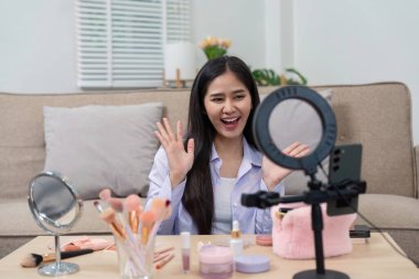 Canlı bir güzellik komisyoncusu, çeşitli makyaj ürünleri ve halka ışığıyla çevrelenmiş canlı yayında seyircisini büyük bir gülümsemeyle selamlıyor..