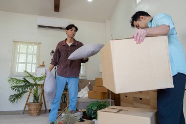 Two men working together to unpack pillows and boxes in their new home, showcasing teamwork and excitement as they create a comfortable living space. clipart