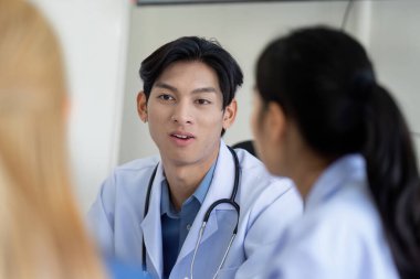 Bir doktor, bir sağlık planlama toplantısı sırasında meslektaşlarıyla klinik bir ortamda hasta bakımı ve stratejileri üzerine ortak bir tartışmaya girişir..