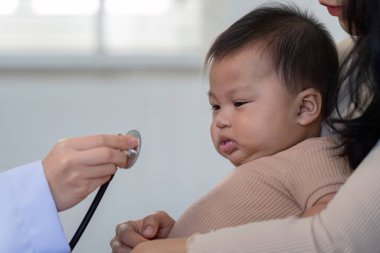 A pediatrician is checking the heart rate of a baby being held by a mother in a medical clinic, ensuring the childs health and safety. clipart