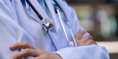 Close up of a doctor arms crossed, wearing a white coat and stethoscope, representing professionalism and commitment in the medical field. clipart