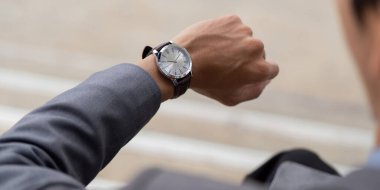 Takım elbiseli genç bir Asyalı işadamının yakından görünüşü, saatini kontrol etmesi, çağdaş bir açık hava ortamında profesyonelliği ve zaman yönetimini yansıtması..