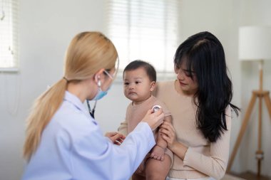 Bir pediyatrist, bebeğini muayene etmek için steteskop kullanır. Annesinin yakından izlediği gibi. Klinik bir ortamda dikkatli ve eksiksiz bir sağlık kontrolü sağlar..