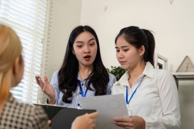 Çeşitli bir iş ekibi, ofis ortamında belgeleri incelerken proje detayları hakkında bir tartışmaya girişir..