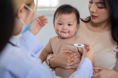 A pediatrician is measuring a baby temperature with a thermometer while the mother holds the smiling infant in a medical clinic, promoting child health. clipart