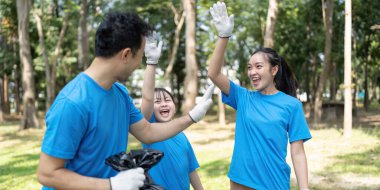 Gönüllülerden oluşan neşeli bir aile, başarılı çöp toplama etkinliklerini bir parkta kutluyor. Takım çalışması ve çevre için coşku sergiliyorlar..