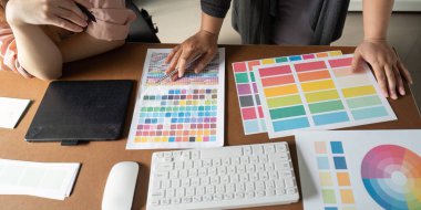 Renk örnekleri ve tasarım materyallerini inceleyen, modern ofis ortamında takım çalışması ve yaratıcılığı ön plana çıkaran iki kadın grafik tasarımcısının genel görünümü.