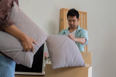 A gay couple packing their belongings, including pillows, into boxes while preparing to move to a new home. clipart