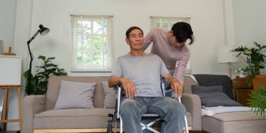 Bir oğul yaşlı babasına evde tekerlekli sandalyede yardım eder, sıcak bir aile ortamında destek ve bakım gösterir..