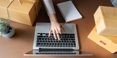 Bilgisayarına yazı yazan ve çevrimiçi satışlarını organize eden kendini adamış Müslüman bir kadın. Yanında paketler ve e-ticarete olan bağlılığını vurgulayan bir defter var..