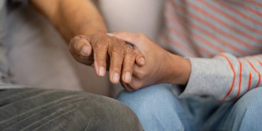 Genç bir adamın yaşlı babasıyla nazikçe el ele tutuşması aile ilişkilerindeki sevgi ve bağlantıyı simgeliyor..