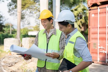 İki lojistik mühendisi, takım çalışması ve proje yönetimini vurgulayan bir inşaat sahasında proje planlarını tartıştı.