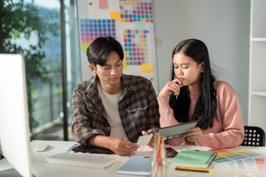 Çeşitli grafik tasarım ekibi, modern ve yaratıcı bir çalışma alanında işbirliği yaparken bir tablette proje ayrıntılarını ve renk şemalarını analiz ediyor..