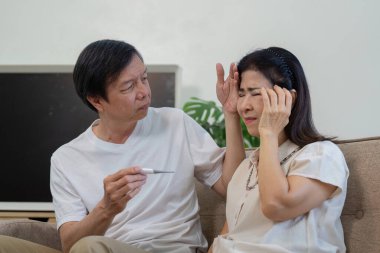 Evde yaşlı bir çift, bir partneri termometre tutarken, diğeri için endişeleniyor..