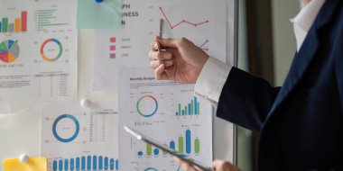 Yaşlı bir işadamı elinde bir kalemle mali tablolara işaret ederek, karar verme sürecindeki verilerin önemini vurguluyor.