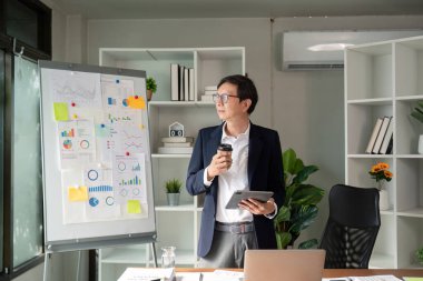 Yaşlı bir profesyonel, mali tabloları incelerken kahve yudumlar, rahatlama ve işyerinde odaklanmayı temsil eder..