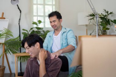 A gay couple shares a laugh while giving each other a massage, enjoying their time together as they settle into their new home. clipart