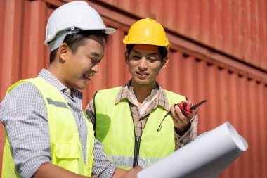 Mühendisler, etkili iletişim için planlar ve bir telsiz kullanarak inşaat lojistiği üzerinde işbirliği yapıyorlar..