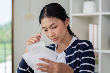 Finansal belgelerini ve faturalarını dikkatlice inceleyen genç bir kadın, bütçe ve finansal okur yazarlığa odaklanıyor..