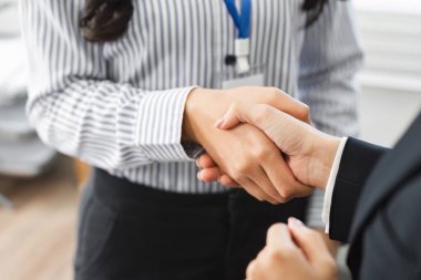 Çağdaş bir ofis ortamında iş dünyası profesyonelleri arasındaki el sıkışma, anlaşmayı ve işbirliğini sembolize eden yakın çekim görüntüsü.