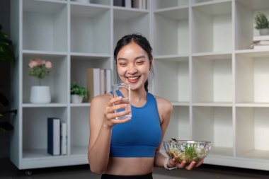 Aktif giyinmiş gülümseyen bir kadın ferahlatıcı bir içecek ve dengeli bir yaşam tarzını temsil eden bir kase salatadan hoşlanır..