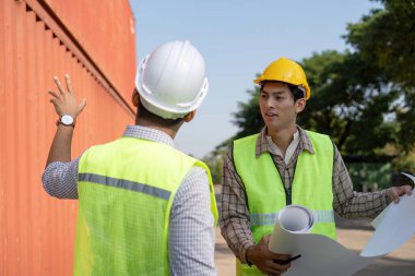 Mühendisler, konteyner yönetimi ve operasyonel verimliliği vurgulayan lojistik bir ortamda inşaat planlarını değerlendiriyor.