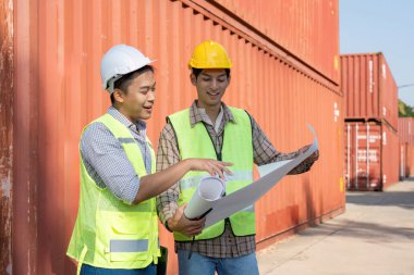Mühendisler, proje yönetimi ve güvenlik protokollerini vurgulayarak bir konteyner deposunda lojistik planlarını analiz ediyorlar..