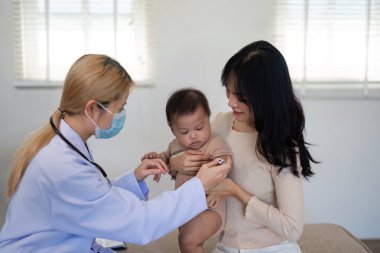 Çocuk doktoru çocuğu klinik ortamında güvenli bir şekilde tutarken bebek sıcaklığını ölçer..
