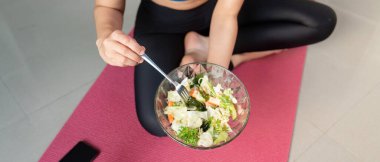 Bir kadın, günlük rutininde sağlıklı beslenme ve zindeliği vurgulayarak bir kase salata tutar..