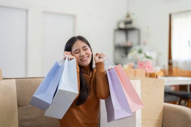 Keyifli genç bir kadın alışveriş poşetleriyle poz veriyor, açık ev ortamında online alışverişini sergiliyor..