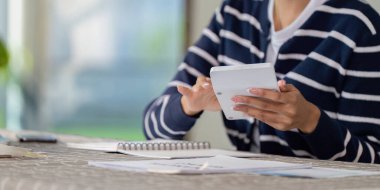 Bir kişi, organize belgeler ve notlarla çevriliyken finansal planlama ve faturaları yönetmek için dijital tablet kullanıyor.