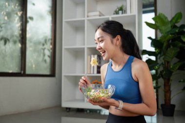 Neşeli bir kadın bir kase salatadan zevk alır ve aktif bir yaşam tarzında sağlıklı beslenmenin önemini vurgular..