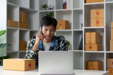 Genç bir girişimci, ürün kutularıyla dolu modern bir çalışma alanında dizüstü bilgisayar kullanırken çevrimiçi satışları yönetiyor..